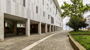 Un bâtiment moderne avec un long couloir, de grandes fenêtres et un arbre au premier plan.
