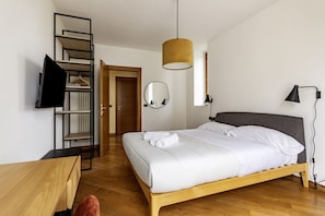 A bedroom with a bed, a wooden desk, a mirror, a hanging light fixture, and a wardrobe with a mirror.