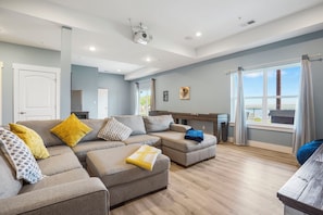 A modern living room with a sectional sofa, a wooden coffee table, and a large window with curtains.