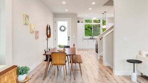 Une cuisine moderne avec des meubles blancs, une table à manger en bois et une vue sur l’extérieur.