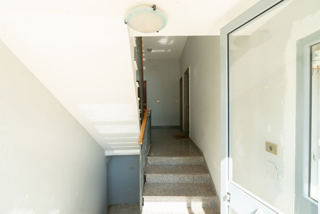 A narrow stairway with a handrail, a light fixture at the top, and a door on the right.
