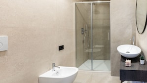 A modern bathroom with a glass-enclosed shower, a white pedestal sink, and a wooden vanity with a mirror.
