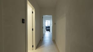 A narrow hallway with a door on the left and a bathroom visible in the distance.