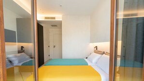 A hotel room with a bed, a mirror, a door, and a light fixture.