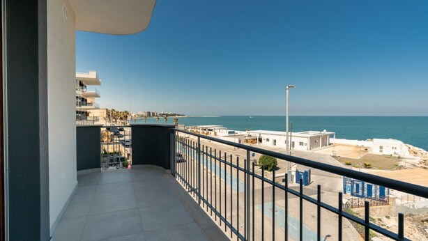 A balcony with a view of the sea, a parking area, and a building with a white facade. - GuestHost –La Rosa dei Venti, Borea Apt by the sea (Trani)