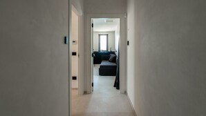 A narrow hallway leading to a living area with a sofa and a window. - GuestHost –La Rosa dei Venti, Borea Apt by the sea (Trani)