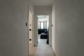 A narrow hallway leading to a living area with a sofa and a window.