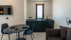 A compact kitchen with a dining area, a flat-screen TV, and a view of the sea through a window. - GuestHost –La Rosa dei Venti, Borea Apt by the sea (Trani)