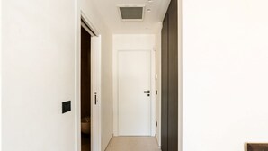 En hall med en vit dörr, en ventilationsöppning i taket och en ljusströmbrytare på väggen.