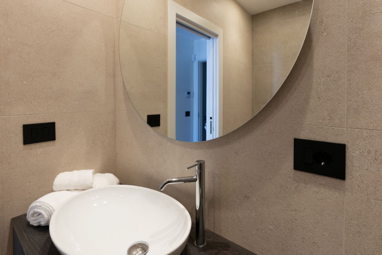 A bathroom with a round mirror, a white sink, and a towel on the counter.