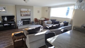 Een woonkamer met een bank, een salontafel, een open haard, een televisie en een eethoek met stoelen.