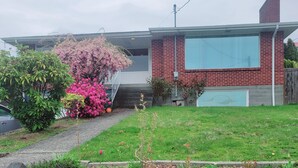 Een tweelaags bakstenen huis met een groot raam op de tweede verdieping, een zichtbare schoorsteen en een klein voortuintje.