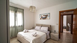 Ein Schlafzimmer mit Bett, Nachttischen, einer Hängelampe, einem Bild eines Bootes und einer Tür.