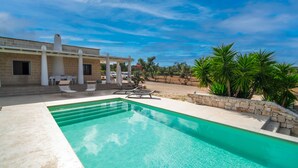 Ein Swimmingpool mit Liegestühlen, einer überdachten Terrasse und Blick auf eine Wüstenlandschaft.