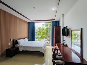 A modern hotel room with a wooden panel wall, a large bed, a desk with a chair, a flat-screen TV, and a large window with curtains. - LE'S HOTEL & APARTMENT (Da Nang)