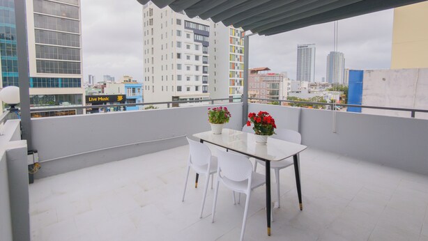 A rooftop terrace with a table and chairs, potted plants, and a cityscape view. - LE'S HOTEL & APARTMENT (Da Nang)