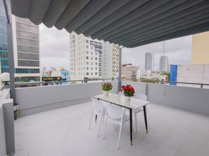 A rooftop terrace with a table and chairs, potted plants, and a cityscape view. - LE'S HOTEL & APARTMENT (Da Nang)