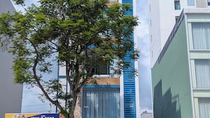 A hotel named "LE'S HOTEL - APARTMENT" with a modern facade, large windows, and a tree in front. - LE'S HOTEL & APARTMENT (Da Nang)