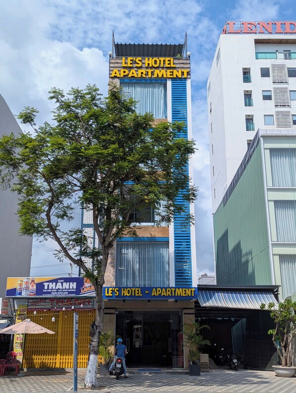 A hotel named "LE'S HOTEL - APARTMENT" with a modern facade, large windows, and a tree in front. - LE'S HOTEL & APARTMENT (Da Nang)
