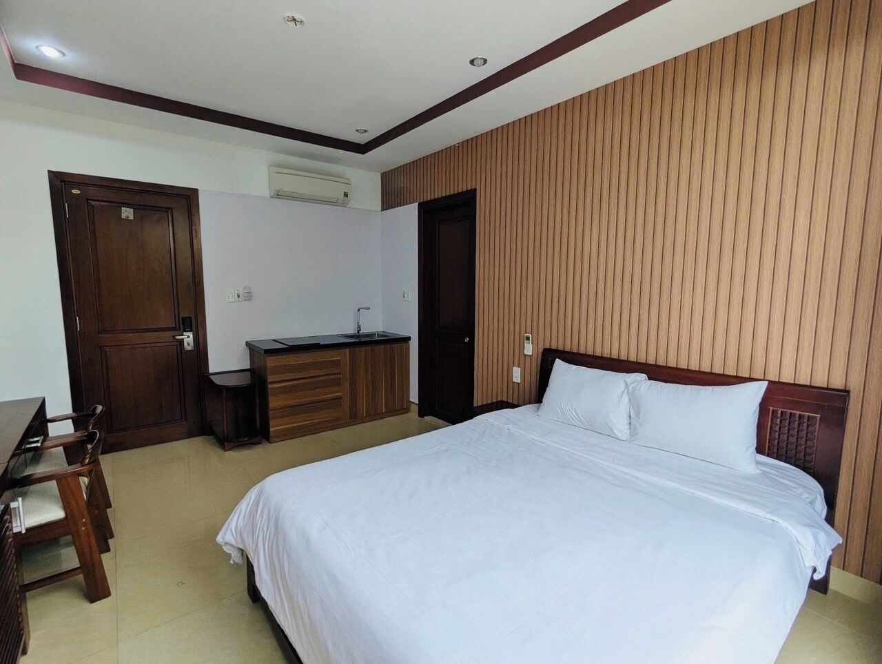 Habitación de hotel con una cama grande, paneles de madera en las paredes, un escritorio con una silla y una pequeña cocina.