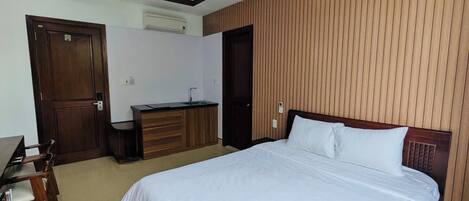 Habitación de hotel con una cama grande, paneles de madera en las paredes, un escritorio con una silla y una pequeña cocina.