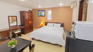 A hotel room with a bed, a desk with a chair, a wardrobe, a bedside table with a lamp, a microwave, and a window with blinds. - LE'S HOTEL & APARTMENT (Da Nang)