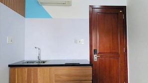 A kitchen with a wooden cabinet, a black countertop, a sink, and a door. - LE'S HOTEL & APARTMENT (Da Nang)