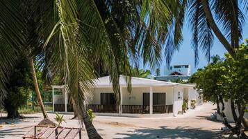 A beachside building with a sandy ground, palm trees, and a clear blue sky.