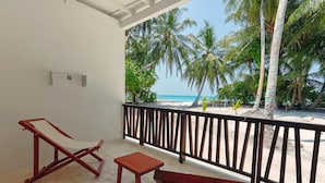 Een balkon met een houten bankje, een kleine tafel en een houten stoel. Het balkon heeft uitzicht op een strand met palmbomen en de oceaan.