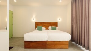 Een tweepersoonsbed met een houten hoofdbord, twee groene kussens en een lichtkleurig tapijt.
