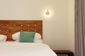 Ein ordentlich bezogenes Bett mit Holzkopfstück, einem Nachttisch und einer Wandleuchte.