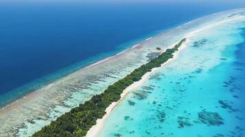 An aerial view of a coastal area with a long stretch of beach, clear turquoise waters, and dense green vegetation along the shoreline.