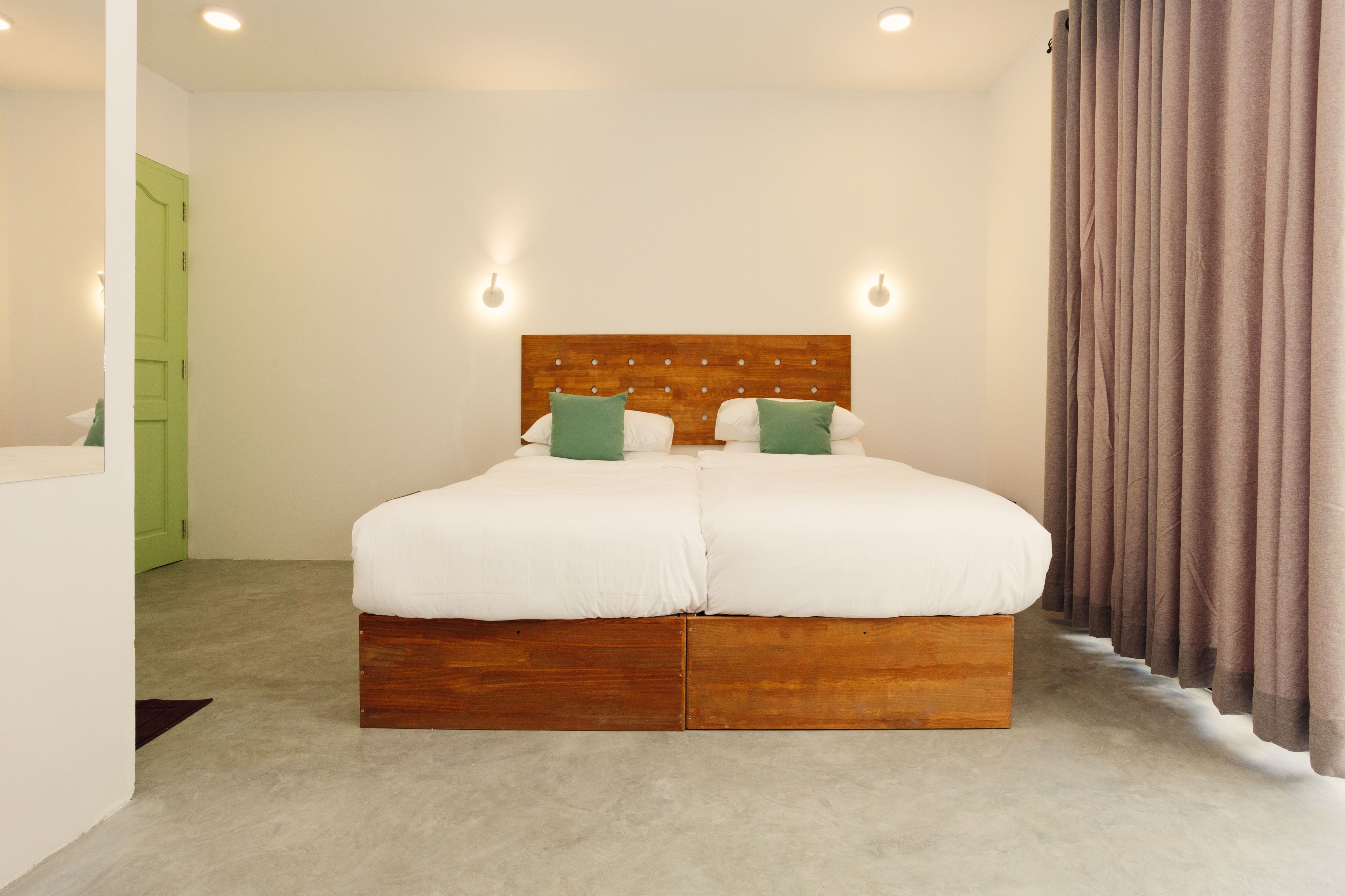 A double bed with a wooden headboard, two green pillows, and a light-colored carpet.