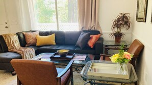 Un salon avec un canapé de couleur foncée, une table basse en verre, un fauteuil en cuir marron et une petite table d’appoint sur laquelle est posé un vase de fleurs.