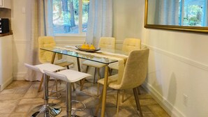 Un coin repas avec une table en verre, des chaises blanches et un lustre.