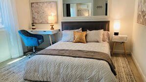 Une chambre d’hôtel avec un grand lit, un bureau, une chaise, un miroir et une table de chevet avec une lampe.