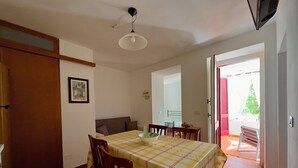 A dining area with a table set for two, a sofa, and a door leading to a balcony.