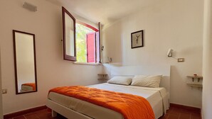 A bedroom with a bed, a window, a mirror, and a wall-mounted light fixture.