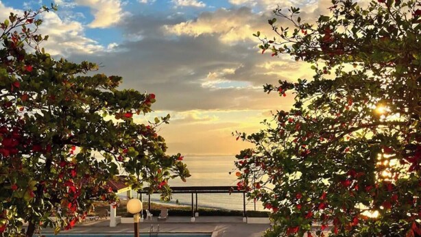 Une piscine offrant une vue sur le coucher de soleil sur l’eau, entourée d’arbres et dotée d’une terrasse.