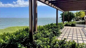 Un espace extérieur abrité, avec vue sur la mer, entouré de verdure et agrémenté d’une pergola.