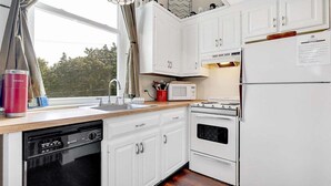 Una cocina con alacenas blancas, lavavajillas, microondas, estufa y refrigerador.