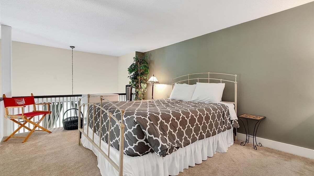 A bedroom with a bed, a chair, a lamp, and a plant.