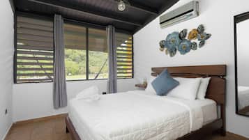 A bedroom with a bed, curtains, an air conditioner, and a wall decoration.