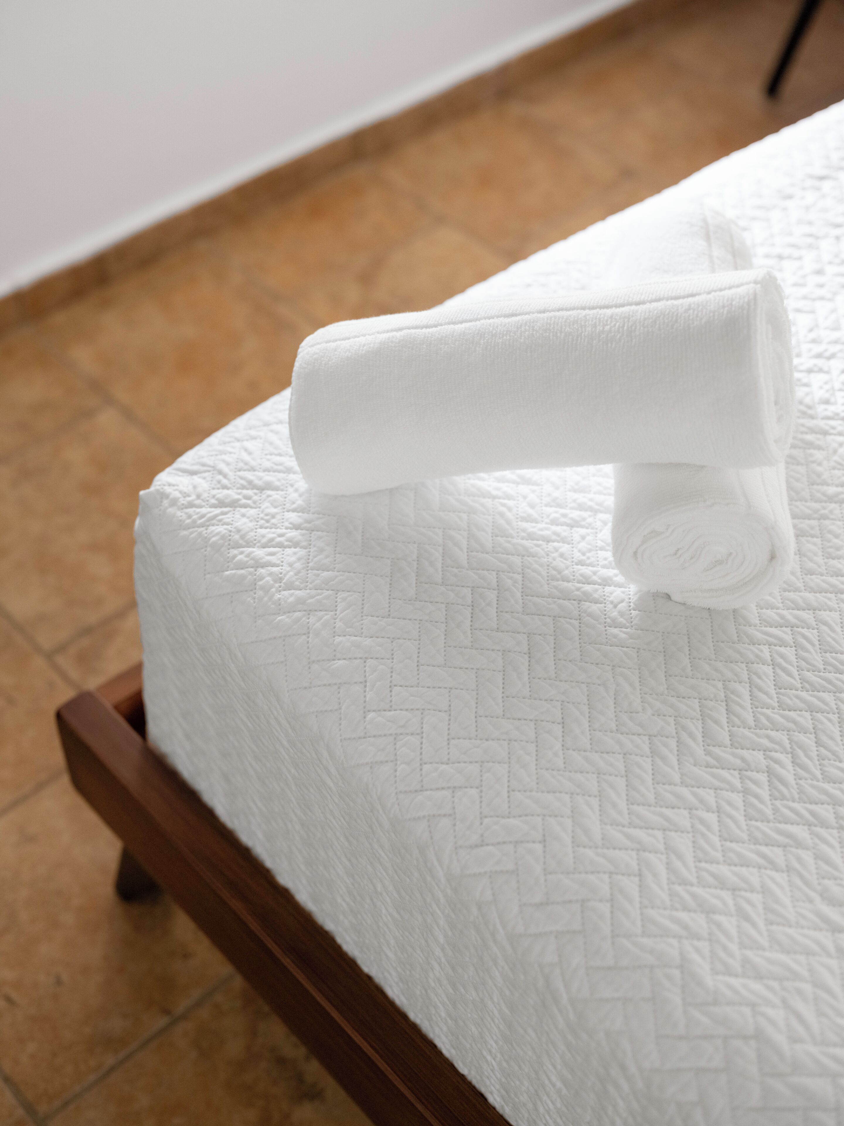 A neatly made bed with a quilted white mattress and a wooden frame.