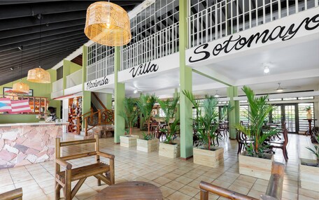 A spacious lobby with high ceilings, wooden furniture, and potted plants.