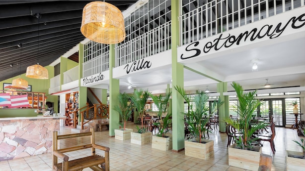 A spacious lobby with high ceilings, wooden furniture, and potted plants.