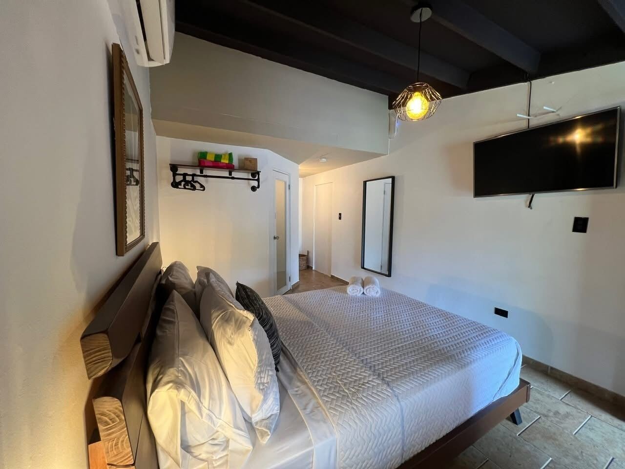 A bedroom with a bed, a TV, a mirror, and a shelf with decorative items.