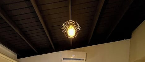 Un dormitorio con una cama grande, dos mesitas de noche con lámparas, una lámpara de techo, un equipo de aire acondicionado y una obra de arte enmarcada en la pared.