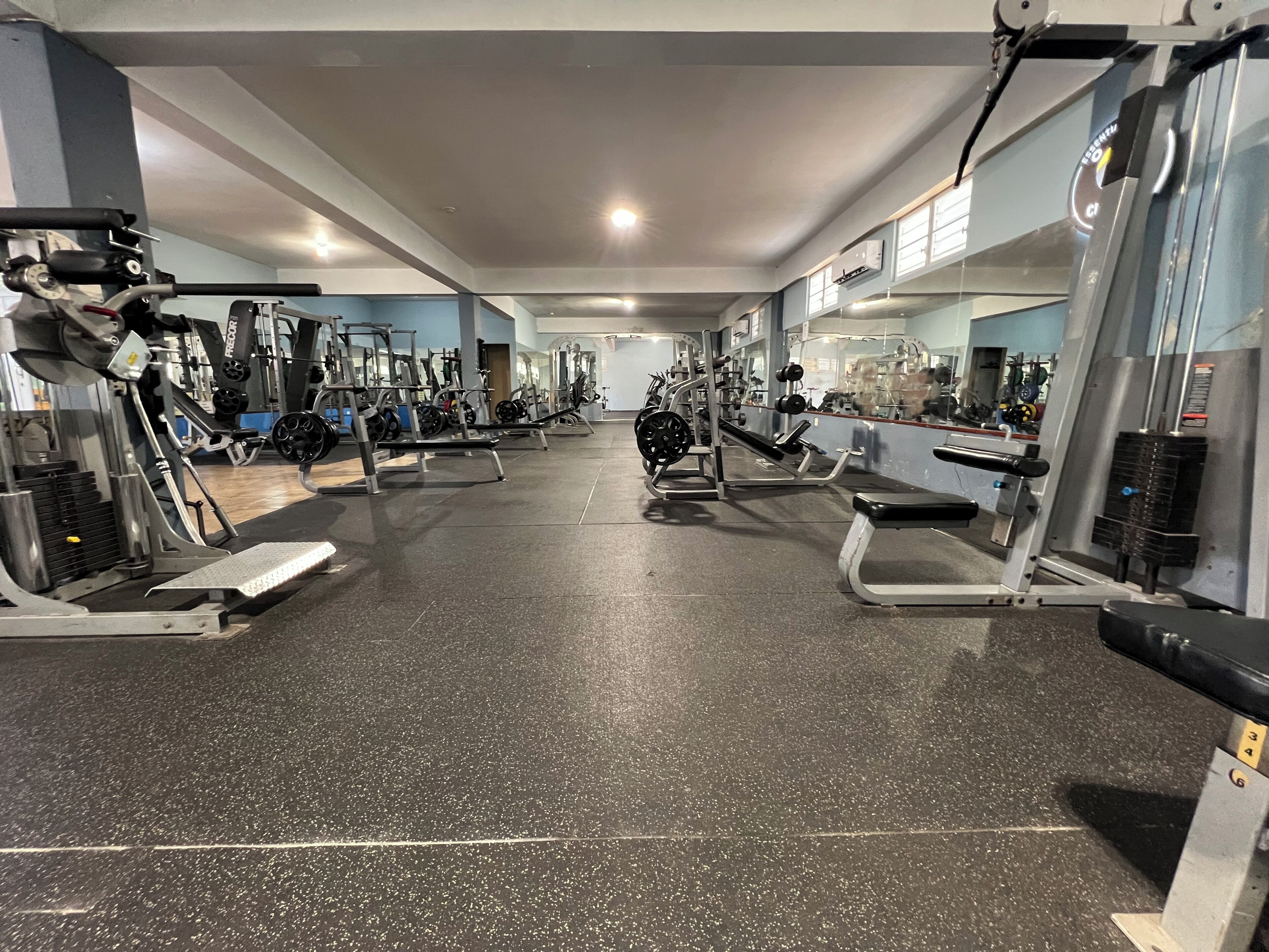 A gym with various exercise machines, a mirrored wall, and a speckled floor.