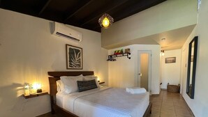 A bedroom with a wooden bed, a bedside table with a lamp, an air conditioner, and a wall-mounted shelf with decorative items.